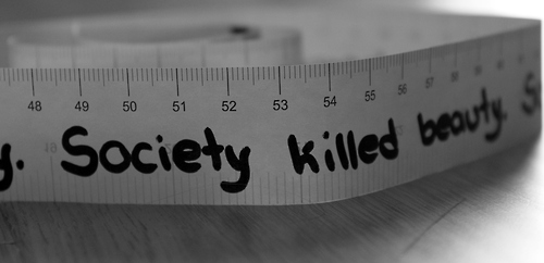 measuring tape lays on a table with the words 'society killed beauty' written on it in thick black marker