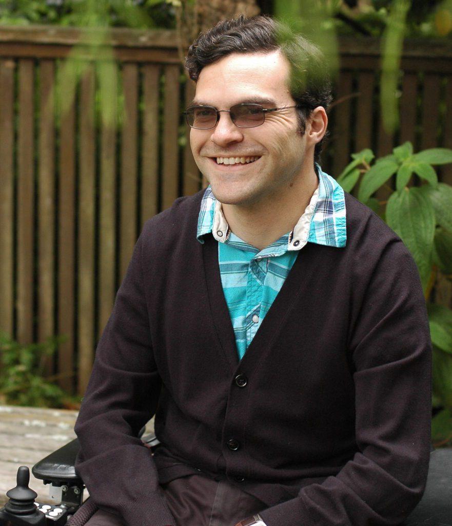 male therapist Michael MacLafferty sits in his wheelchair, smiles broadly looking off camera